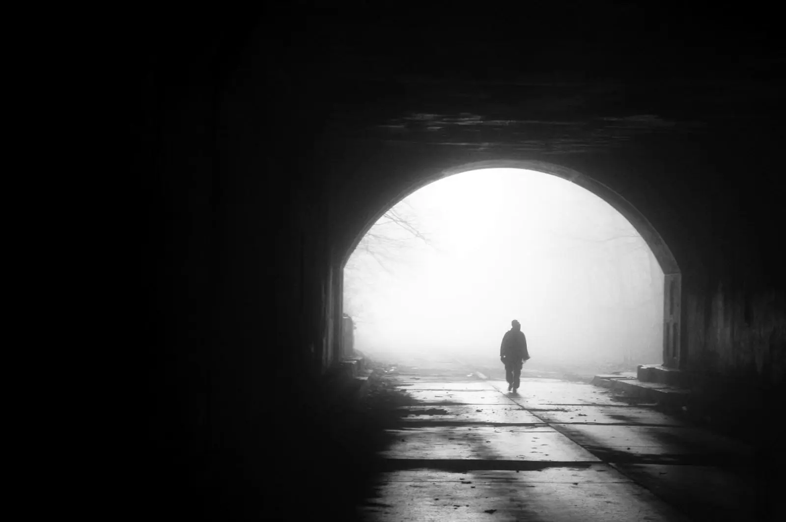 A lone figure walking out of a dark tunnel towards daylight.
